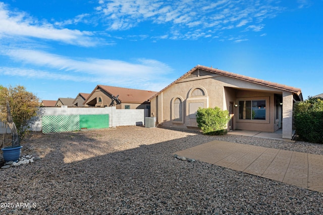 exterior space with a tile roof, stucco siding, central AC unit, and fence