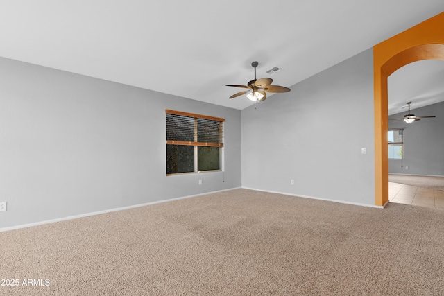 spare room featuring baseboards, light colored carpet, vaulted ceiling, arched walkways, and a ceiling fan