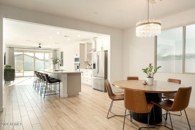 dining area with sink, ceiling fan with notable chandelier, and light wood-type flooring