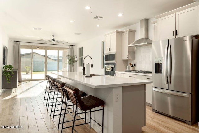 kitchen featuring sink, wall chimney range hood, stainless steel appliances, and an island with sink