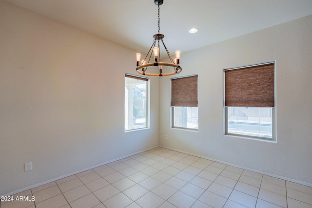 tiled spare room featuring an inviting chandelier