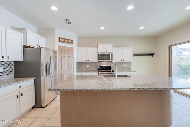 kitchen with an island with sink, light stone counters, appliances with stainless steel finishes, and sink