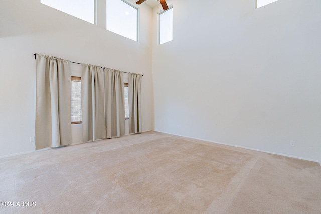 spare room featuring ceiling fan, light colored carpet, and a high ceiling