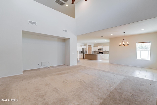 unfurnished living room featuring ceiling fan with notable chandelier, a high ceiling, and light colored carpet