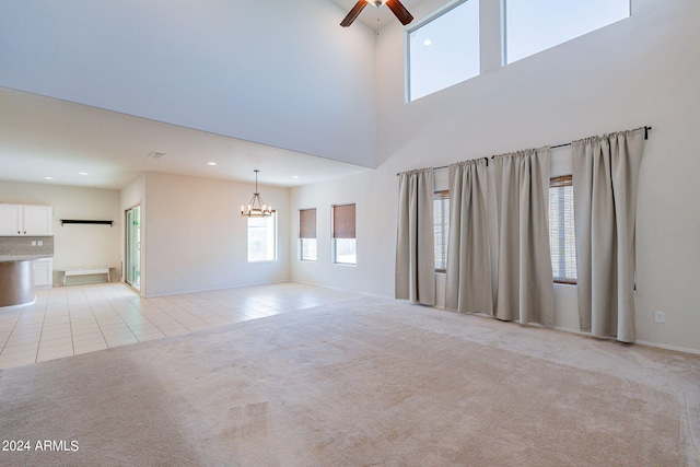 unfurnished living room with ceiling fan with notable chandelier, a high ceiling, and light carpet