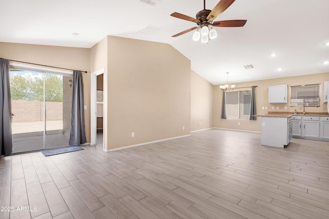unfurnished living room featuring visible vents, baseboards, light wood-style flooring, ceiling fan with notable chandelier, and vaulted ceiling
