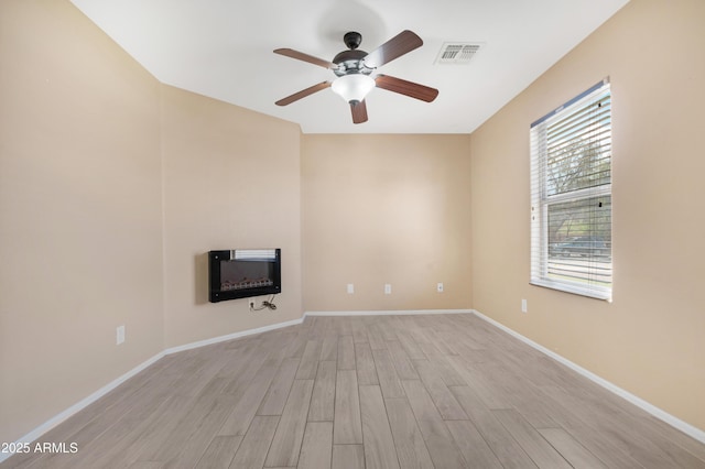 unfurnished living room with ceiling fan, visible vents, a glass covered fireplace, light wood finished floors, and heating unit
