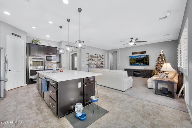 kitchen featuring ceiling fan, sink, stainless steel appliances, hanging light fixtures, and a center island with sink