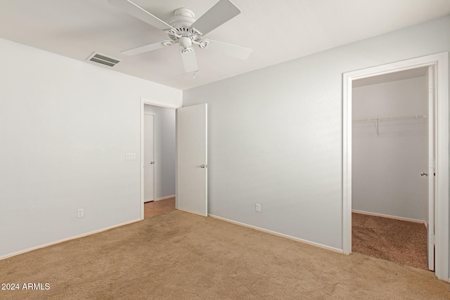 unfurnished bedroom featuring a closet, light colored carpet, a walk in closet, and ceiling fan