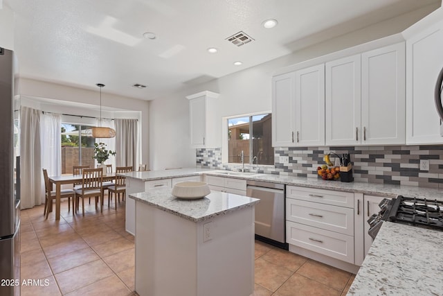 7736 W Tumblewood Dr, Peoria, AZ 85382 - kitchen with appliances with stainless steel finishes, decorative backsplash, a kitchen island, light tile patterned flooring, and white cabinets
