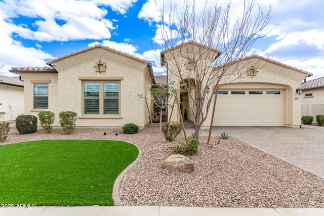 mediterranean / spanish-style house with decorative driveway, a tiled roof, an attached garage, and stucco siding