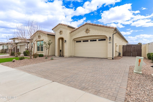 mediterranean / spanish-style home featuring decorative driveway, an attached garage, a gate, and stucco siding