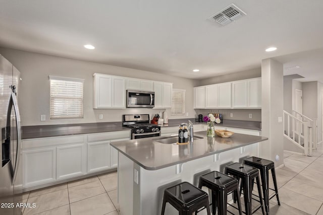 kitchen featuring a breakfast bar area, stainless steel appliances, a sink, visible vents, and white cabinets