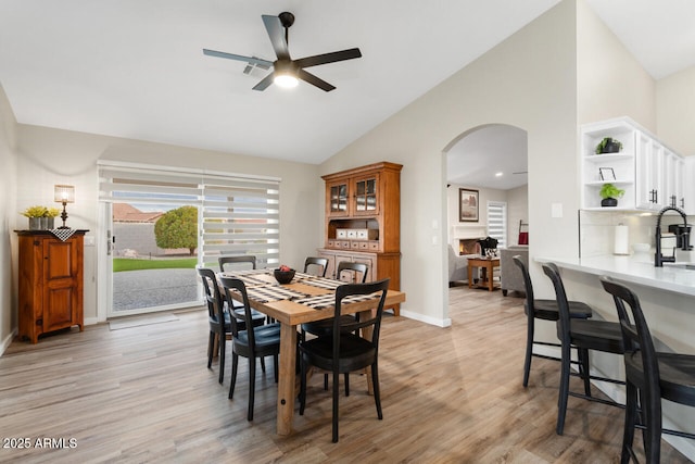 dining space featuring light hardwood / wood-style floors, a large fireplace, ceiling fan, and vaulted ceiling