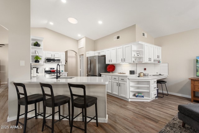 kitchen with kitchen peninsula, sink, white cabinetry, lofted ceiling, and stainless steel refrigerator