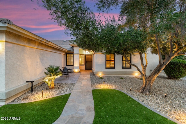 exterior entry at dusk featuring a lawn and a patio