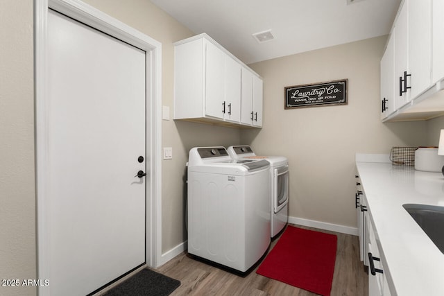 clothes washing area featuring washing machine and clothes dryer, light hardwood / wood-style flooring, and cabinets