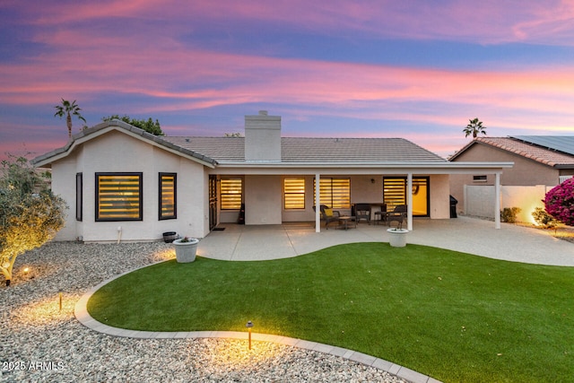 back house at dusk with a patio area and a yard