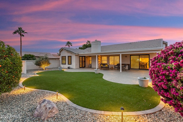 back house at dusk featuring a patio area and a yard