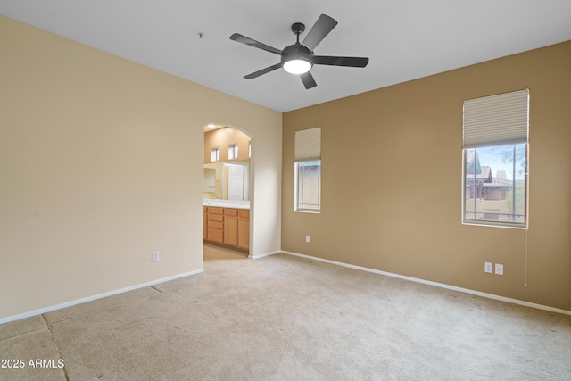 unfurnished bedroom with light carpet, baseboards, arched walkways, ceiling fan, and ensuite bathroom