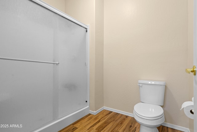 bathroom with toilet, baseboards, wood finished floors, and a shower with shower door