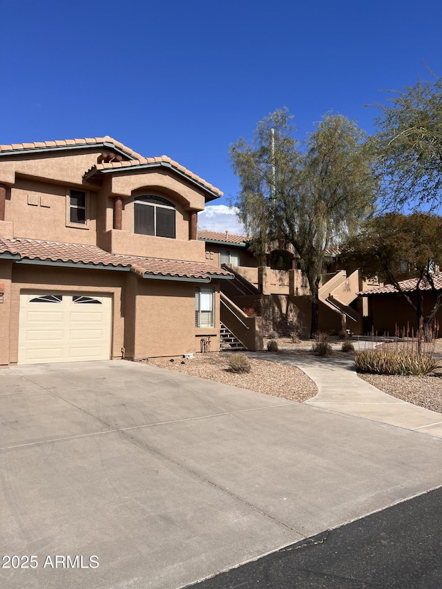 view of front of house featuring a garage, driveway, a tiled roof, and stucco siding