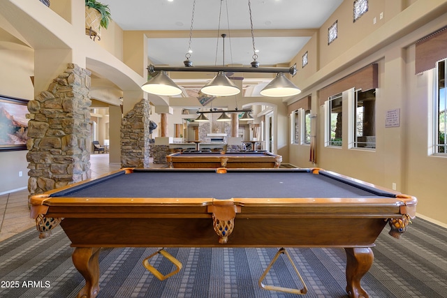 game room featuring arched walkways, baseboards, a towering ceiling, and ornate columns