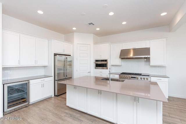 kitchen featuring light wood-type flooring, stainless steel appliances, beverage cooler, sink, and a center island with sink