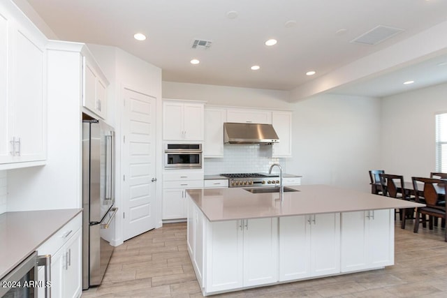 kitchen with a center island with sink, white cabinets, sink, light wood-type flooring, and stainless steel appliances