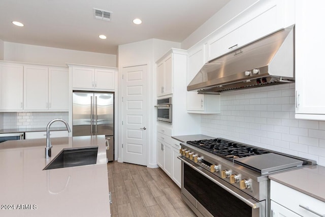 kitchen featuring sink, premium appliances, light hardwood / wood-style flooring, white cabinets, and exhaust hood