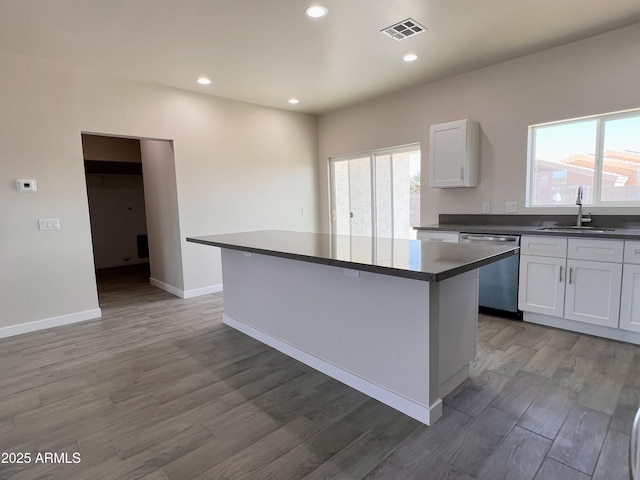 kitchen featuring a sink, visible vents, stainless steel dishwasher, a center island, and dark countertops