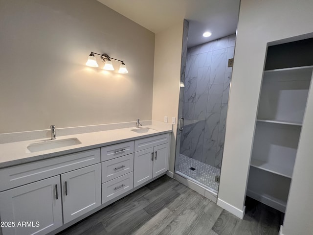 bathroom featuring a spacious closet, a marble finish shower, a sink, and wood finished floors