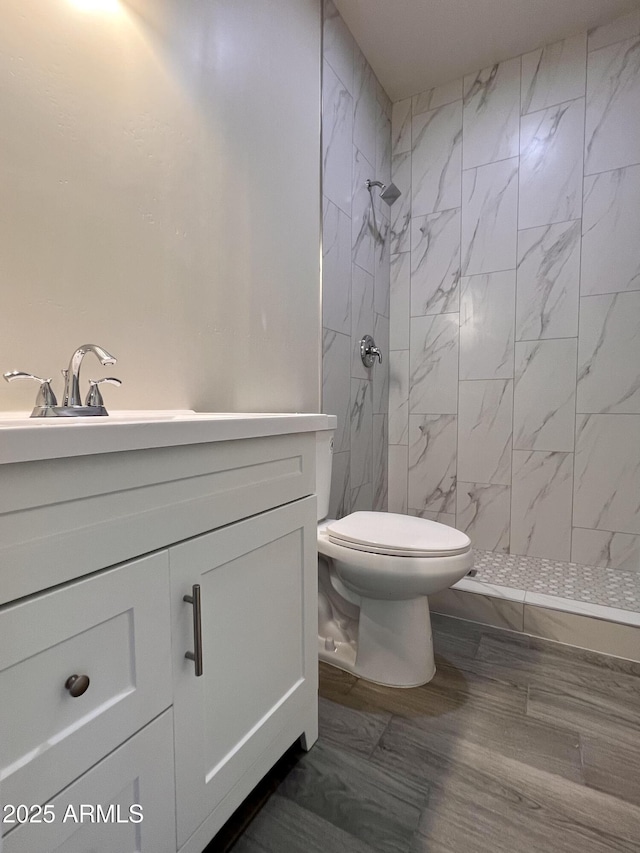 bathroom featuring toilet, a tile shower, and vanity