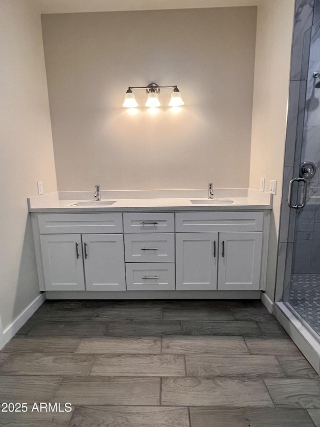 full bath with a stall shower, a sink, baseboards, and double vanity