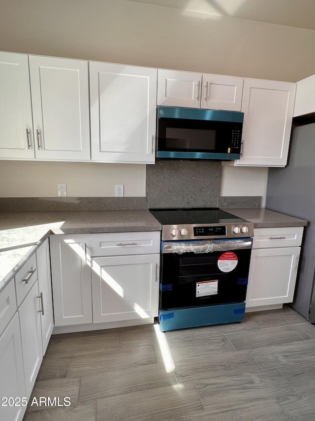 kitchen with freestanding refrigerator, white cabinets, and stainless steel electric range