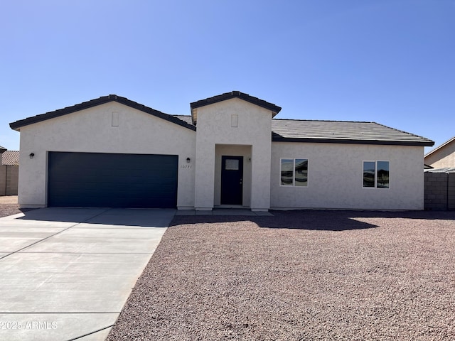 view of front of property featuring a tile roof, stucco siding, concrete driveway, an attached garage, and fence