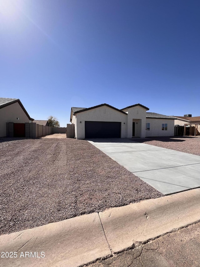 view of front facade featuring concrete driveway, an attached garage, fence, and stucco siding