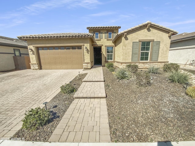 mediterranean / spanish house featuring an attached garage, stucco siding, stone siding, a tile roof, and decorative driveway