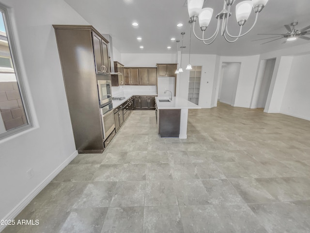 kitchen featuring stainless steel microwave, open floor plan, a center island with sink, light countertops, and a sink