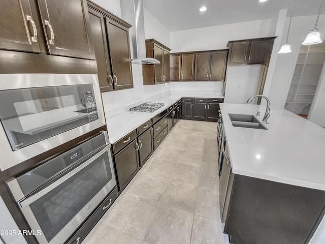 kitchen featuring a sink, stainless steel appliances, light countertops, dark brown cabinetry, and wall chimney range hood