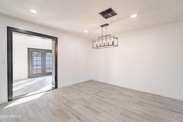 unfurnished dining area featuring french doors, light hardwood / wood-style floors, and a textured ceiling