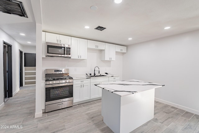 kitchen with white cabinetry, sink, appliances with stainless steel finishes, a kitchen island, and light wood-type flooring