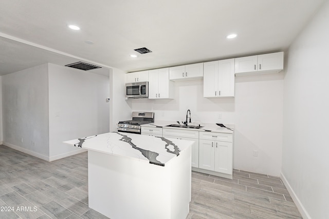 kitchen featuring appliances with stainless steel finishes, sink, light hardwood / wood-style flooring, white cabinets, and a center island