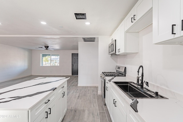 kitchen with appliances with stainless steel finishes, light wood-type flooring, ceiling fan, sink, and white cabinets