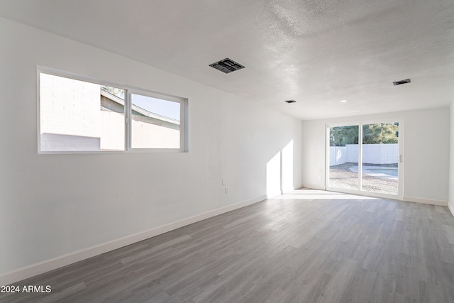 unfurnished room with a wealth of natural light, wood-type flooring, and a textured ceiling