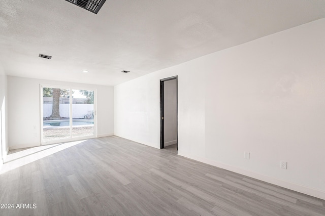 empty room with a textured ceiling and light hardwood / wood-style flooring