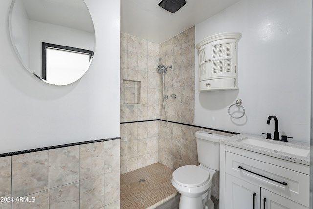 bathroom featuring vanity, toilet, tile walls, and a tile shower