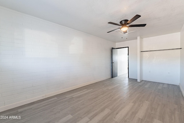 empty room featuring a textured ceiling, light hardwood / wood-style floors, ceiling fan, and brick wall