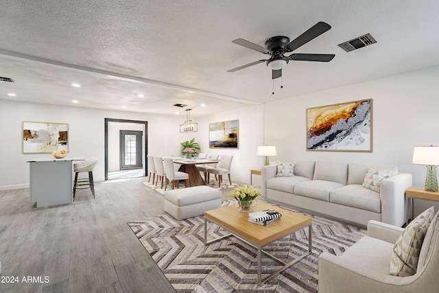 living room with ceiling fan with notable chandelier, light hardwood / wood-style floors, and a textured ceiling