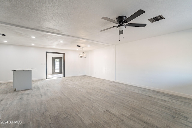 unfurnished room featuring ceiling fan with notable chandelier, a textured ceiling, and light hardwood / wood-style flooring